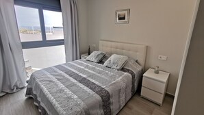A bedroom with a large bed, a nightstand, a framed picture on the wall, and a window with curtains. - Modern Penthouse with a sea view. (Finestrat)