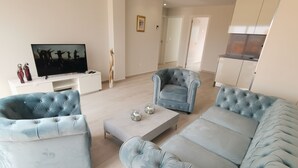A modern living room with a large light blue sofa, two matching armchairs, a coffee table, and a flat-screen TV on a white stand. - Modern Penthouse with a sea view. (Finestrat)