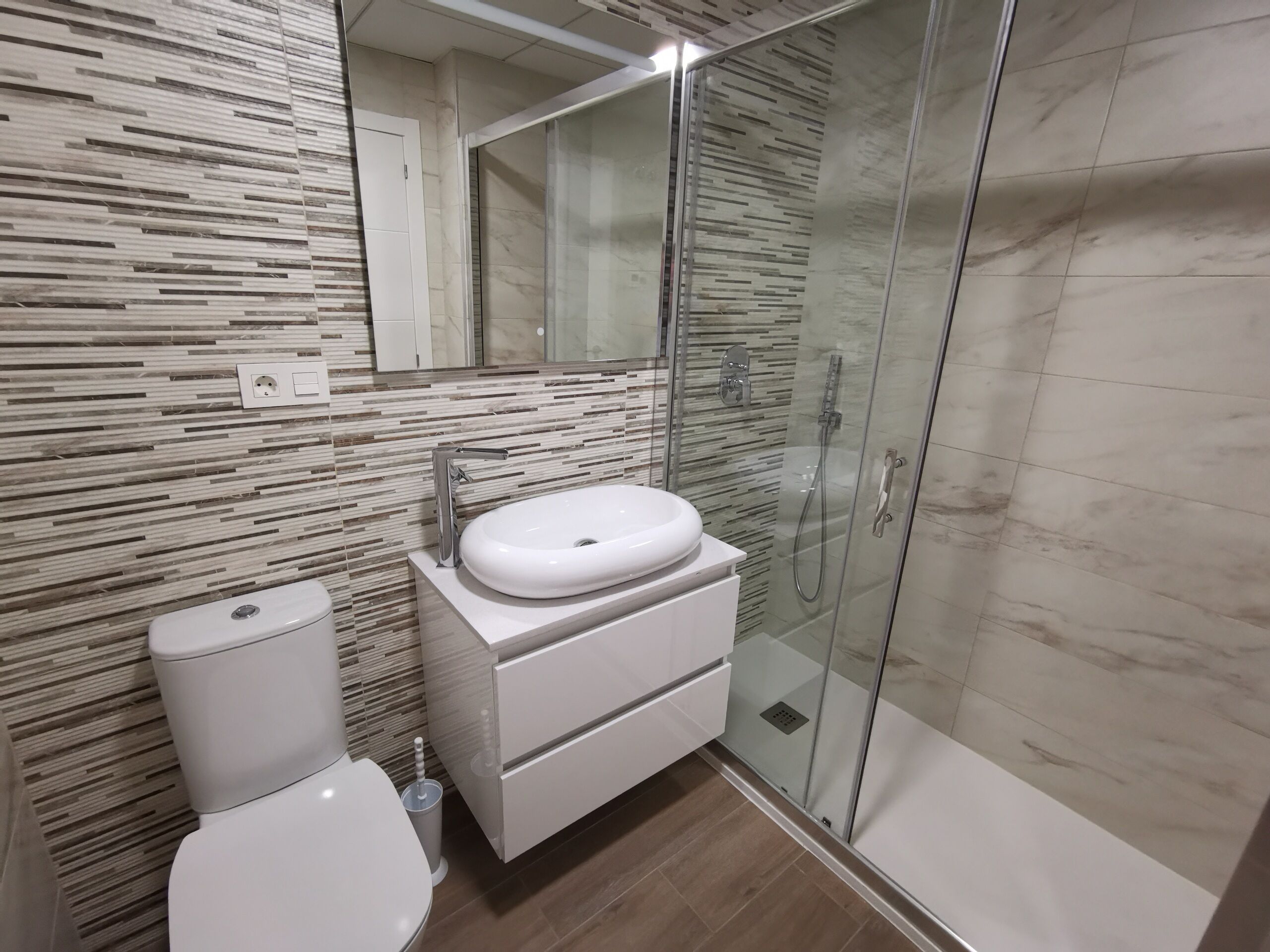 Une salle de bain moderne avec une douche à parois de verre, un lavabo blanc et des toilettes.