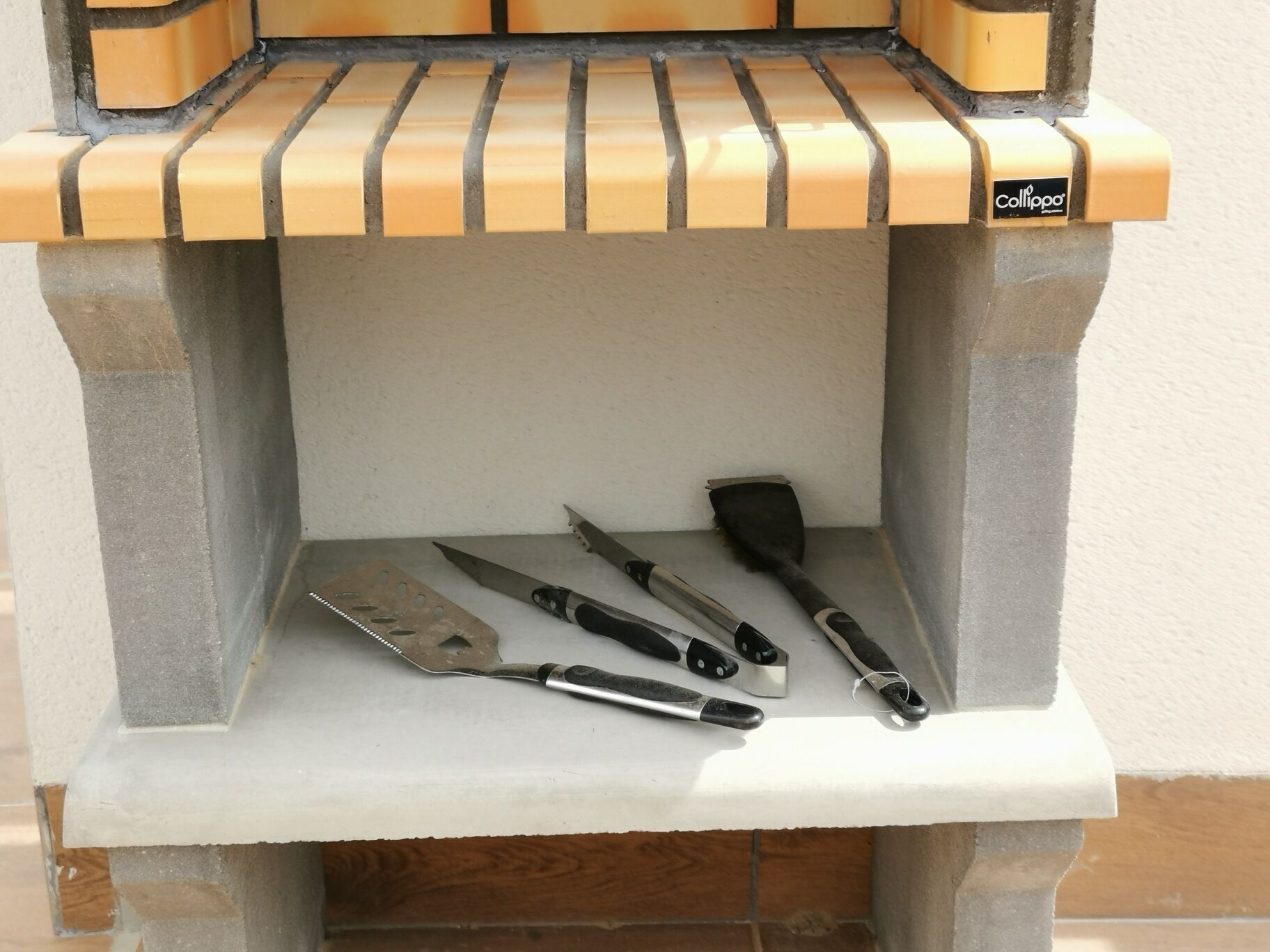 A concrete barbecue grill with a flat top and a shelf for tools.