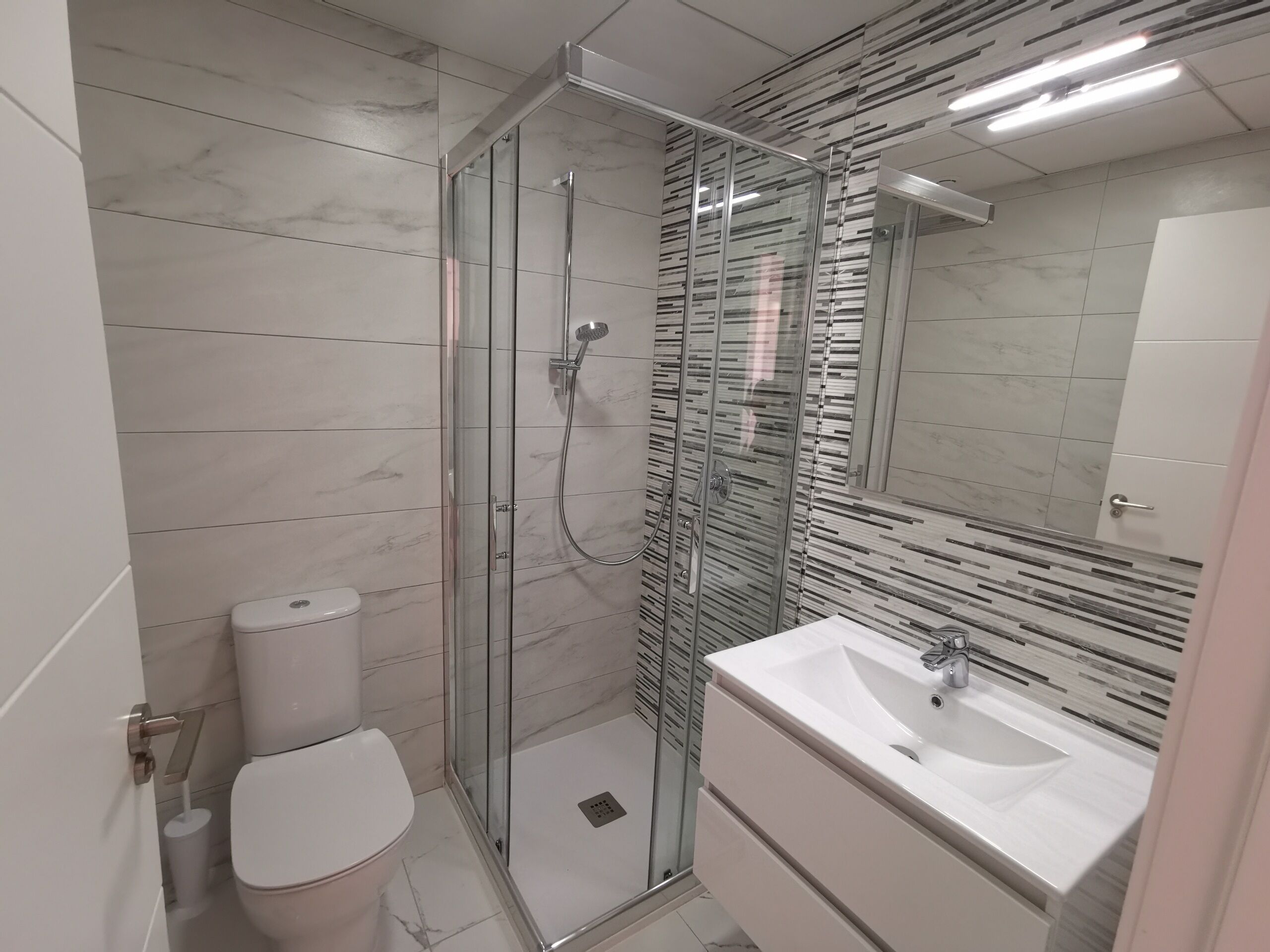 A modern bathroom with a glass-enclosed shower, a toilet, and a sink with a mirror above it.