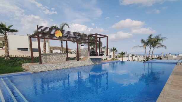 A swimming pool with a wooden deck and a pergola with a sun emblem. - Modern Penthouse with a sea view. (Finestrat)