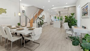 Een moderne eetruimte met een witte tafel voor vier personen, omringd door witte stoelen. Een trap met houten afwerking leidt naar een hoger niveau.