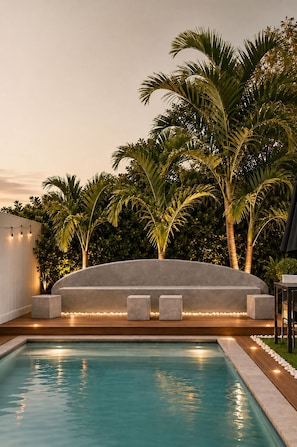 Una piscina con area relax integrata, circondata da palme e un siepe.