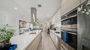 Een moderne keuken met roestvrijstalen apparatuur, een centraal eiland en uitzicht op de eetruimte.