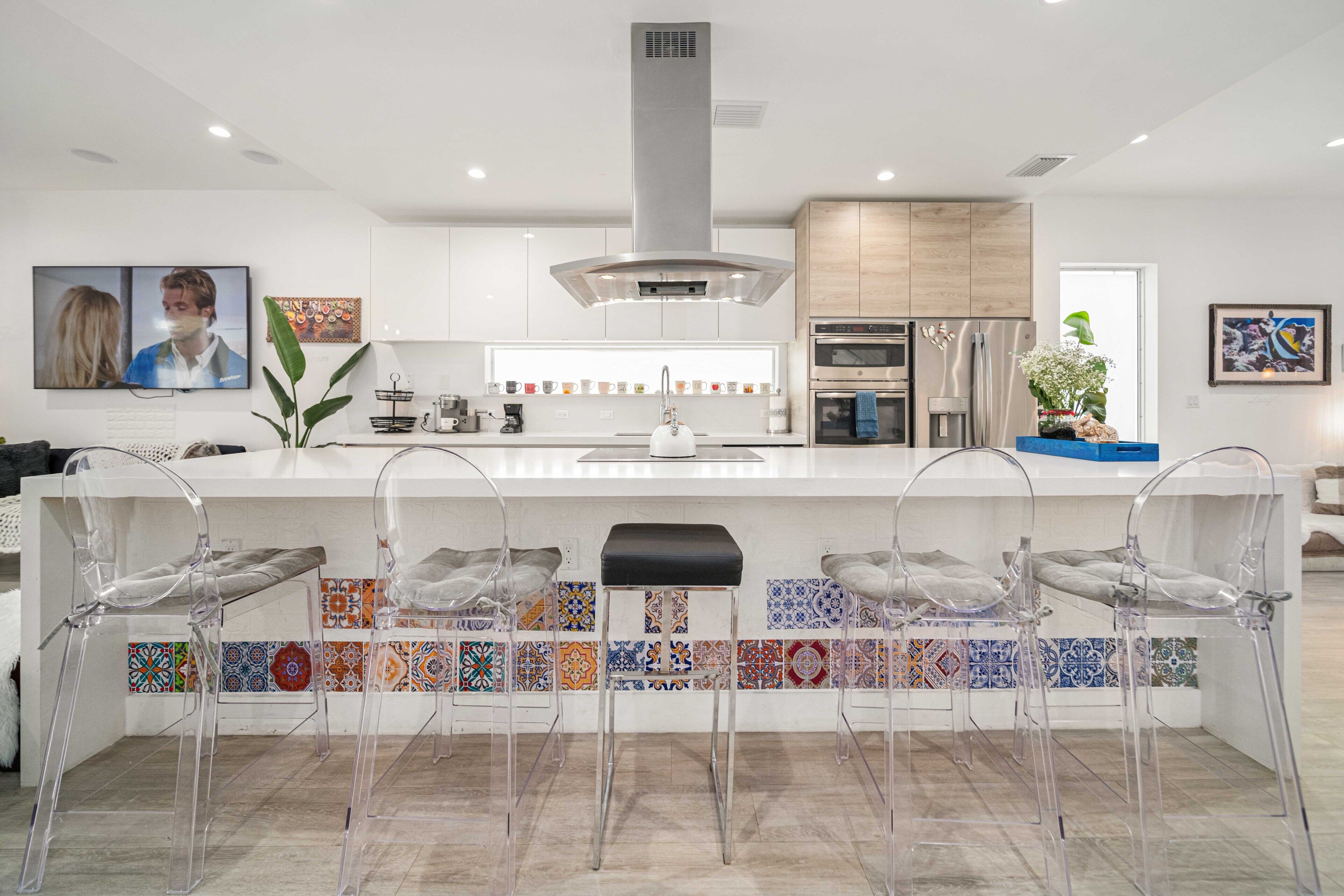 A modern kitchen with a central island, clear chairs, and a tiled backsplash.