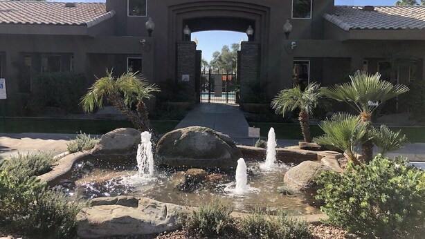 Ein Gebäude mit einem steinernen Bogenportal, einem Wasserspiel mit mehreren Springbrunnen und Palmen.