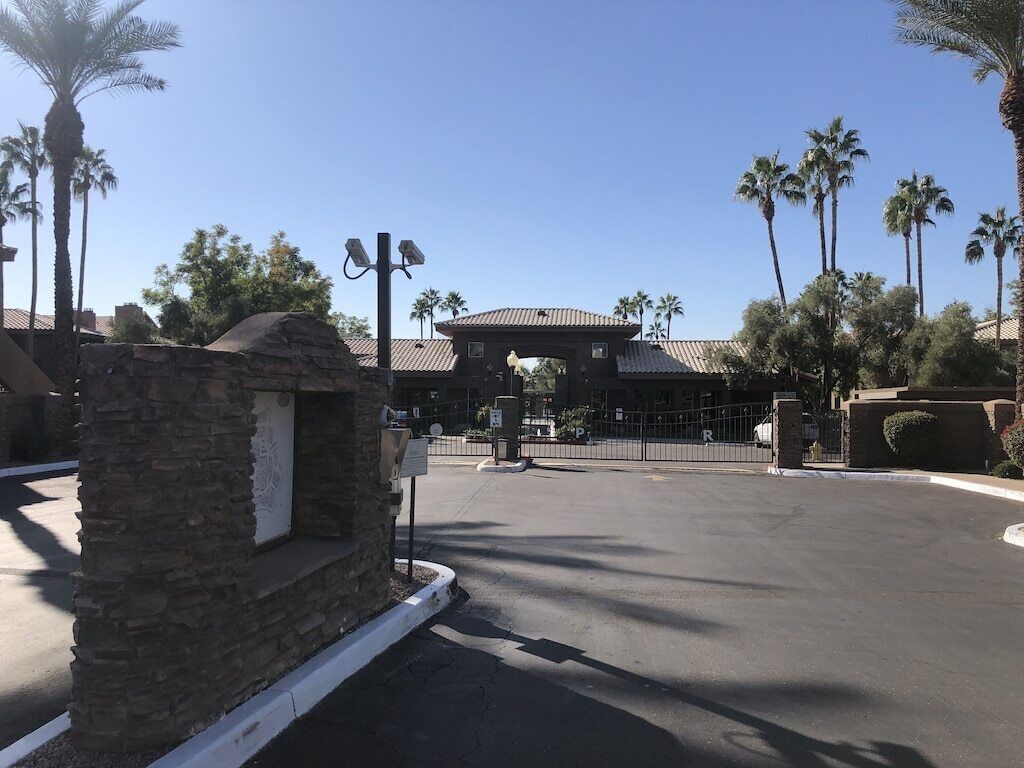 A parking lot with a stone structure, palm trees, and a building with a tiled roof.
