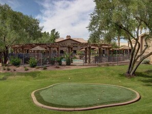 A golf course with a clubhouse, a pool, and a fenced area with trees.