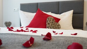 A bed with white and red bedding, a grey upholstered headboard, and decorative heart-shaped pillows. - Amical Hotel Hagen (Hagen)