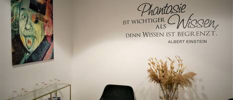 A room with a wall featuring a quote by Albert Einstein, a colorful painting, a glass display case with items, and a vase with dried plants.