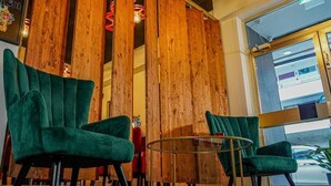 A seating area with two green chairs and a glass table, wooden paneling in the background, and a view through a window. - Amical Hotel Hagen (Hagen)
