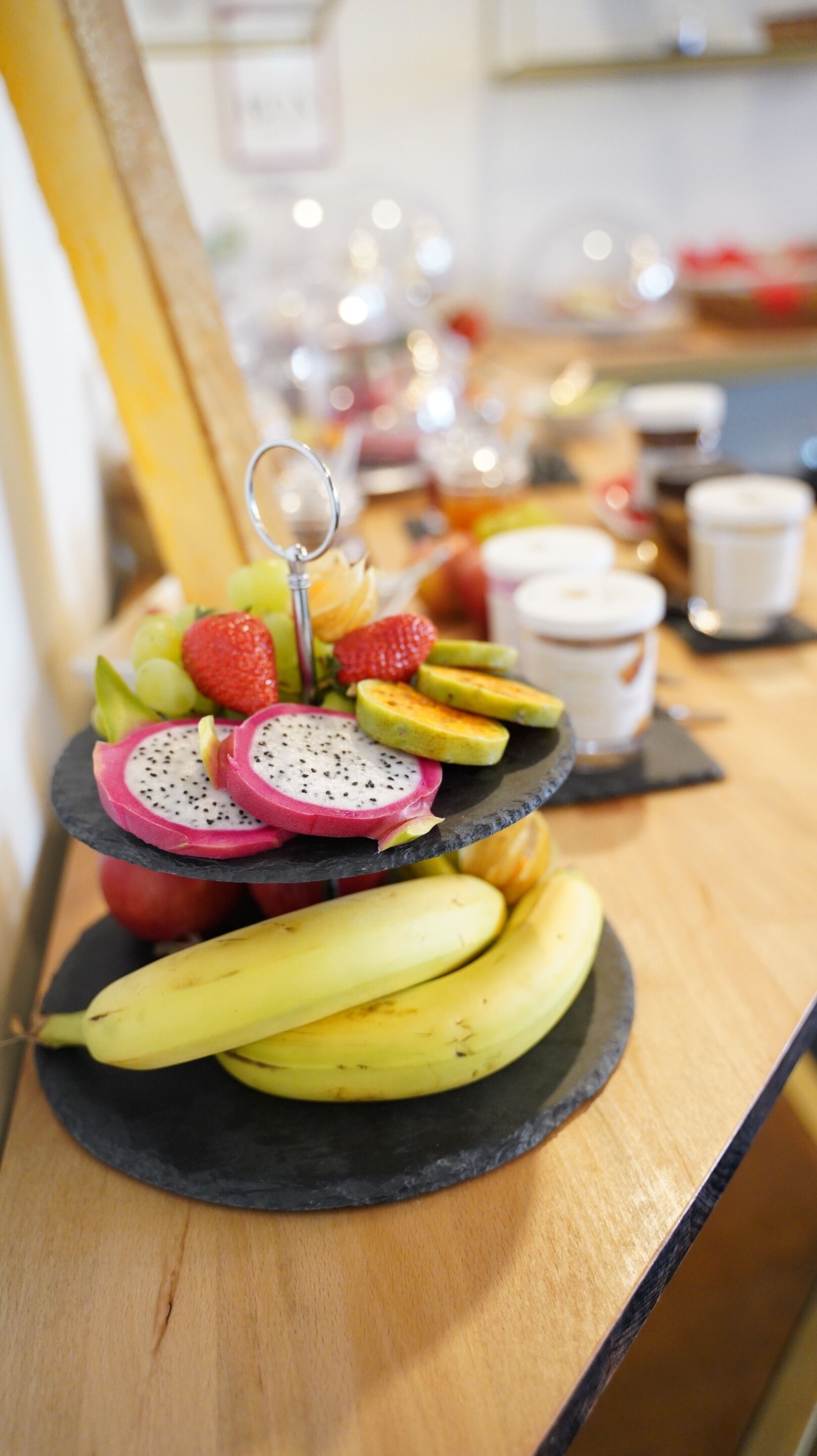 A multi-tiered fruit display with bananas, strawberries, and dragon fruit on a wooden table.