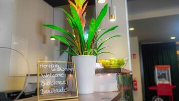 A reception desk with a welcome sign, a potted plant, and a small table with a bowl of fruit.