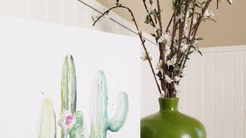 A cactus painting on a wall next to a green vase with branches and flowers.