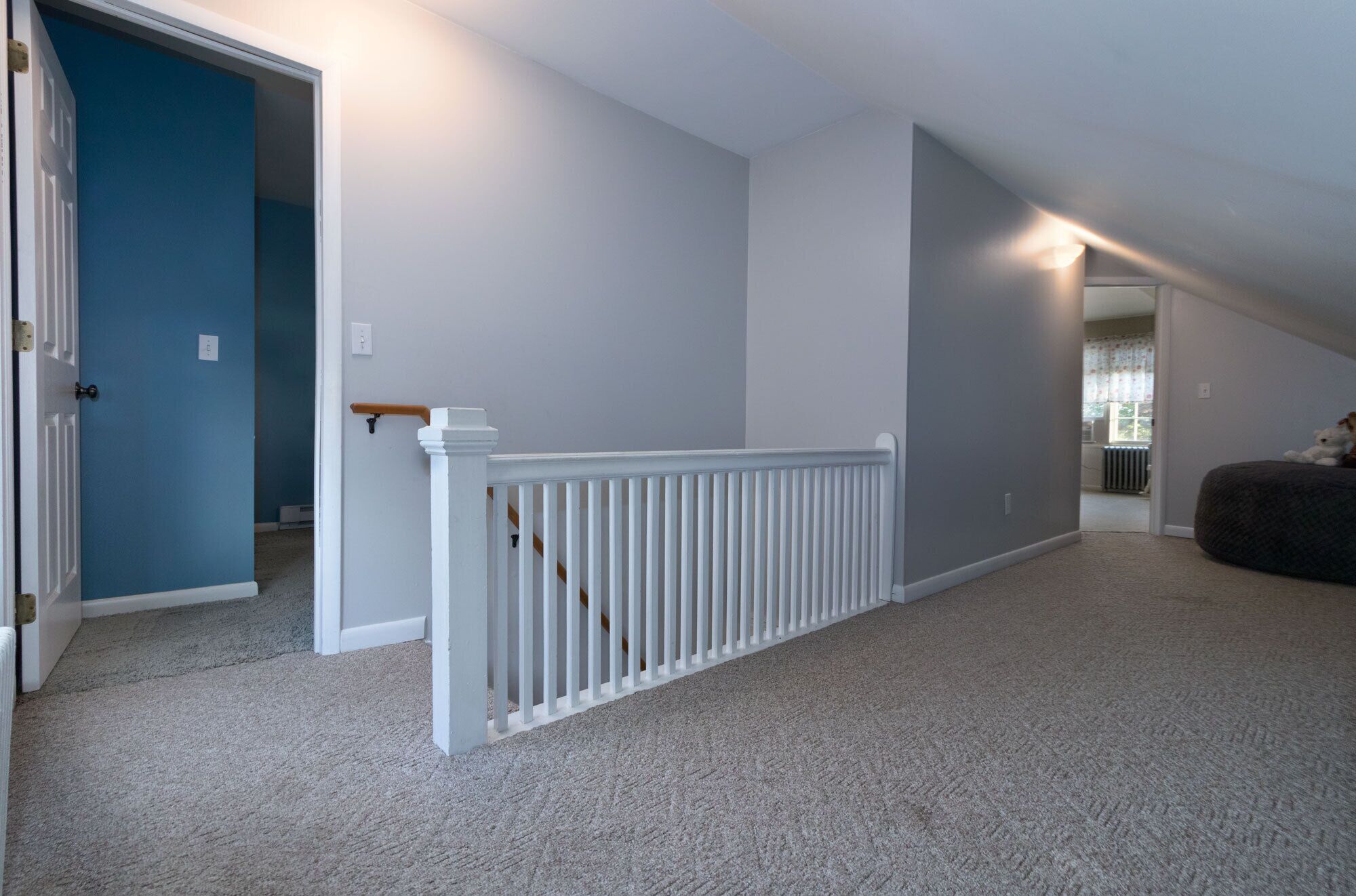 A spacious room with a white railing, a blue door, and a view of a window.