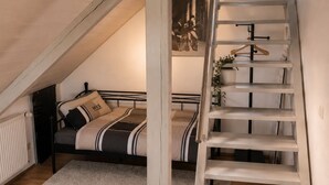 A bedroom with a loft bed, a staircase, and a radiator.