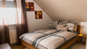 Un dormitorio con techo inclinado, una cama con ropa de cama a rayas, una lámpara de noche y una obra de arte en la pared.