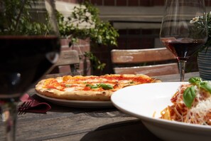 Pizza i un bol de pasta sobre una taula amb un got de vi vermell.