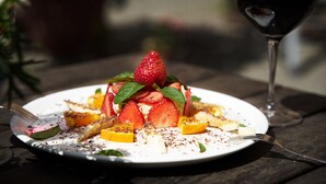 Une assiette de salade de fruits contenant des fraises et de la menthe, ainsi qu'un verre de vin rouge, posée sur une table.