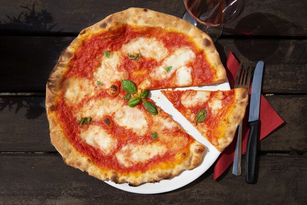 A pizza on a white plate with a slice missing, placed on a wooden table. - two-room WHG in the center (Leipzig)