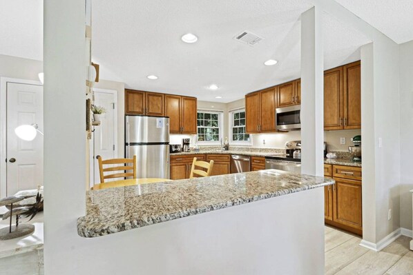 A kitchen with granite countertops, wooden cabinets, stainless steel appliances, and a central island with chairs.