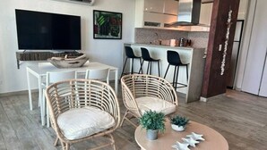 A modern living room with a dining area, a TV, and a kitchen in the background. - Brisa Oceanfront + Beach + Pool + Ocean View Balcony (San Juan)