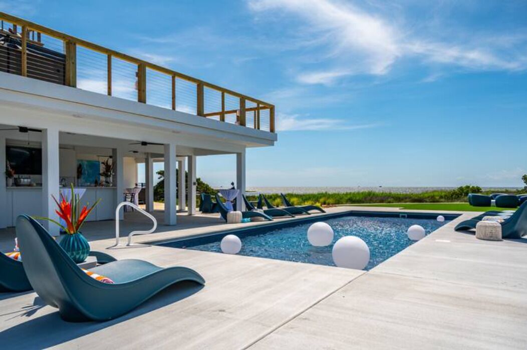 A modern outdoor pool area with lounge chairs, a covered seating area, and a view of the beach.