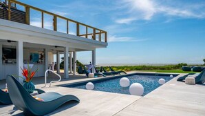 Ein moderner Poolbereich im Freien mit Liegestühlen, einer überdachten Sitzecke und Blick auf den Strand.