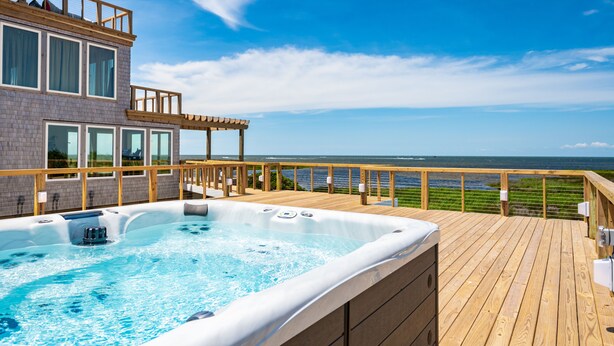 Eine Holzterrasse mit Whirlpool und Blick auf den Ozean.