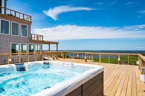 Una terraza de madera con un jacuzzi y vista al océano.