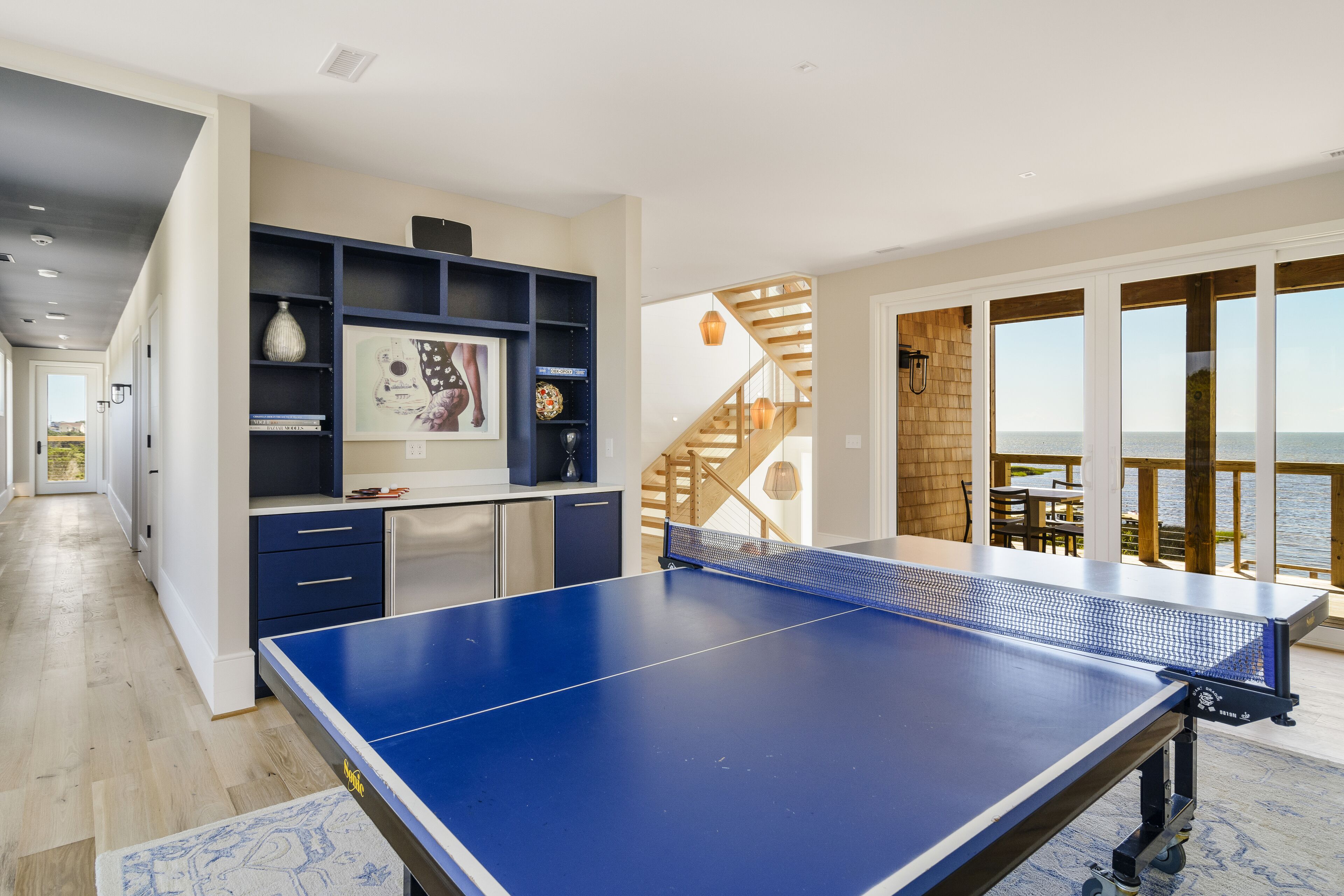 A spacious room with a ping pong table, a built-in shelving unit, and a view of the sea through large windows.