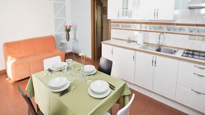 Ein Essbereich mit Tisch für vier Personen, einer Couch und einer Küche mit weißen Schränken und einer gefliesten Spritzschutzwand.