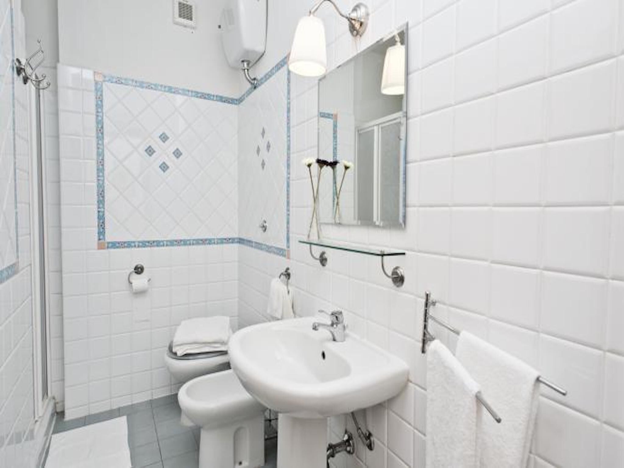 Ein Badezimmer mit weißen Fliesen, einem Waschbecken, einer Toilette und einer Duschkabine.