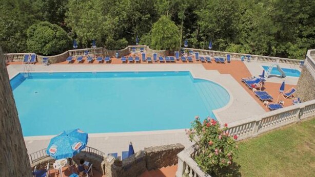 Ein Schwimmbecken mit Liegestühlen und Blick auf einen bewaldeten Gebirgszug.