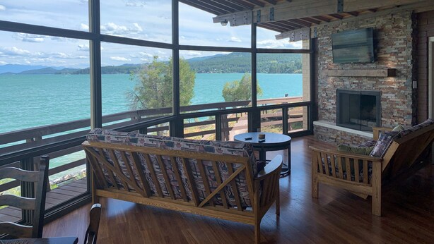 A cozy room with a large window overlooking a lake, a fireplace, and wooden furniture. - PRIVATE ISLAND RETREAT On Gorgeous Flathead Lake Montana!!! (Somers)