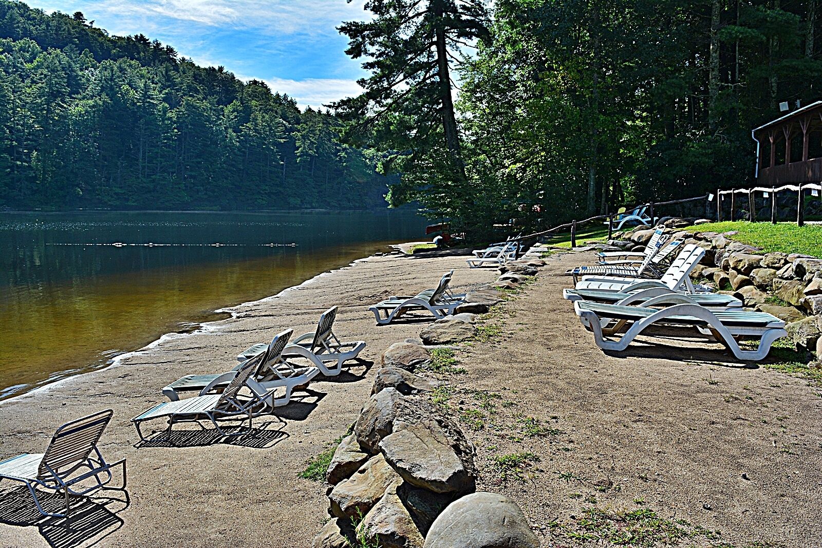 A lakeside beach with lounge chairs and a wooden structure in the background.