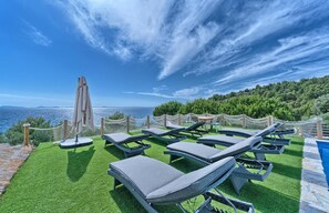 Eine Dachterrasse mit Liegestühlen, einem Tisch und einem Pool mit Blick auf eine malerische Küstenlandschaft.