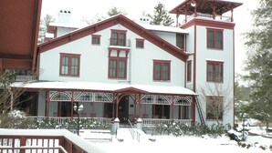 A large, multi-story building with a symmetrical facade, featuring a central entrance with a covered porch and multiple windows with red trim. - Three Cub Cottage in historic Flat Rock (Flat Rock)