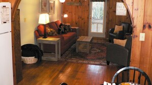 A cozy living room with a wooden interior, a sofa, a coffee table, and a chair. - Three Cub Cottage in historic Flat Rock (Flat Rock)