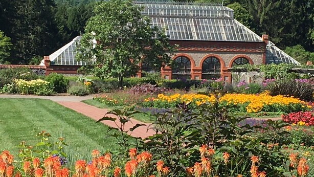 A greenhouse with a glass roof, surrounded by a variety of colorful flowers and a well-maintained garden path. - Three Cub Cottage in historic Flat Rock (Flat Rock)