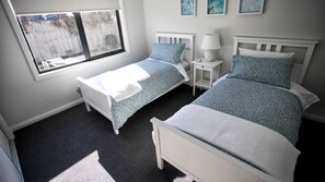 Une chambre avec deux lits, une fenêtre, une table de chevet avec une lampe et une petite étagère.