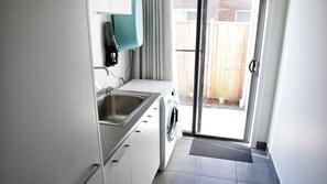 Cocina compacta con lavamanos, lavadora y ventana que da a una valla de madera.