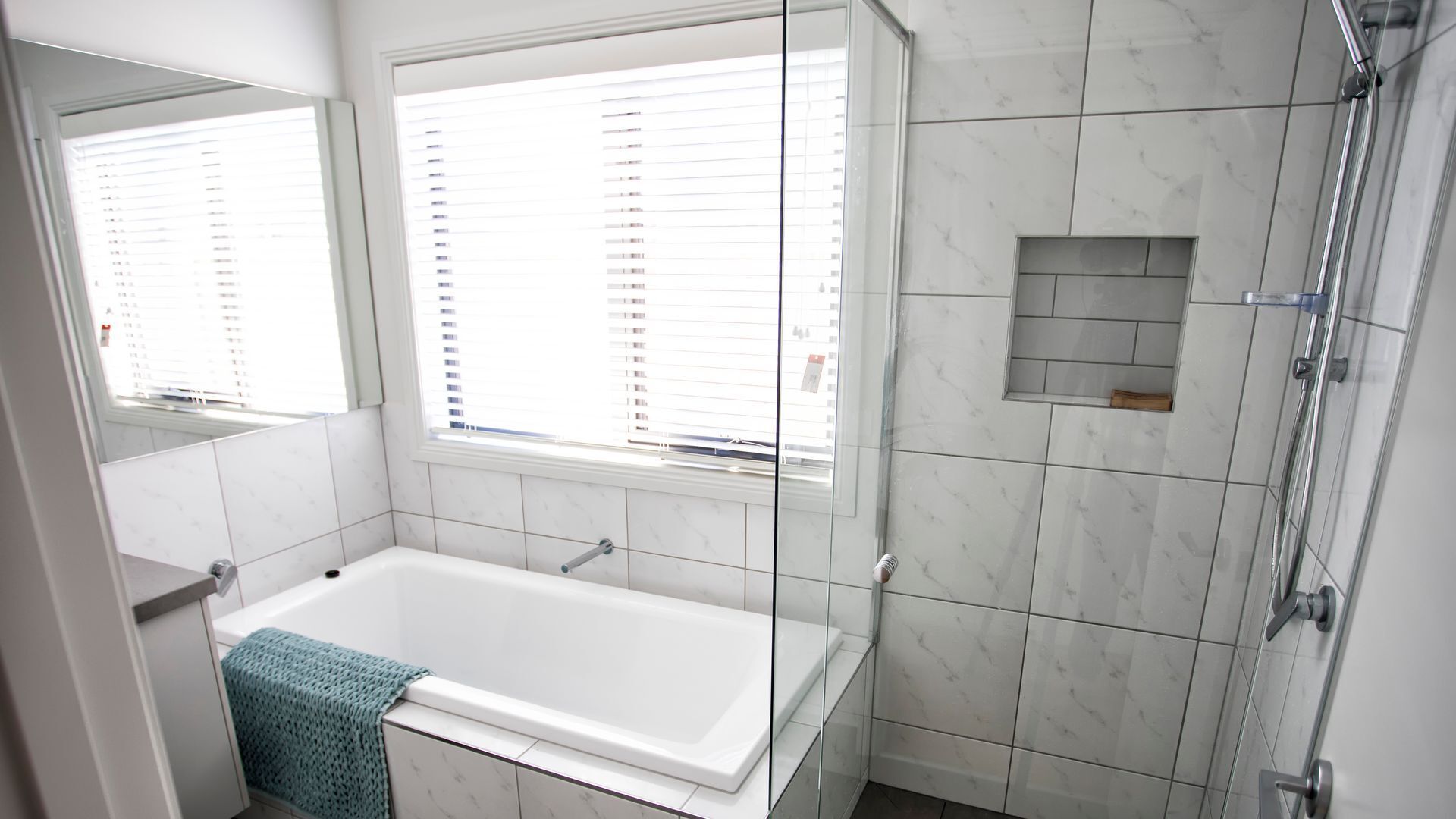 A modern bathroom with a bathtub, a glass shower enclosure, and a window with blinds.