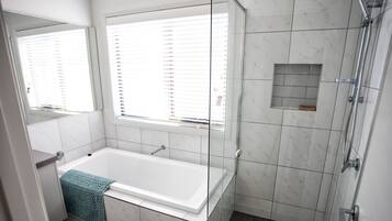 A modern bathroom with a bathtub, a glass shower enclosure, and a window with blinds.