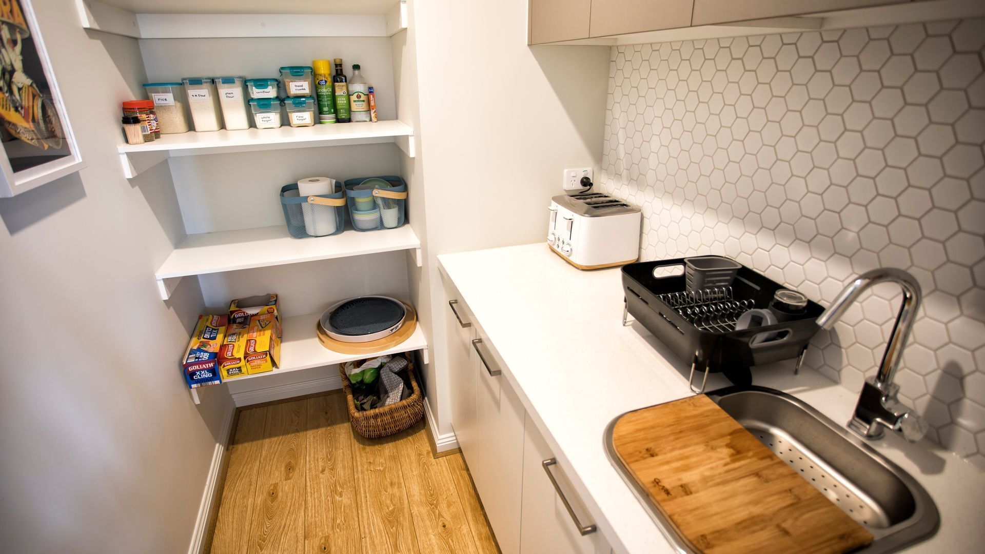 A compact kitchen with a white countertop, a sink, a toaster, and storage shelves with various containers.