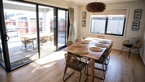 Spiseområde med et træbord og vævede bordskåner, fletstole og udsigt gennem glasdøre til en udendørs terrasse.