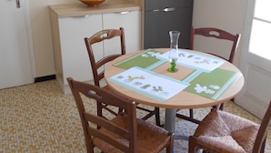 A dining area with a round table, four chairs, a cabinet, and a bowl on the counter. - Gîte Le Penten (Villeréal)