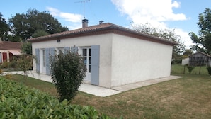 A small, single-story building with a white exterior and a tiled roof. It has a small porch with a door and windows, and a tree in front. - Gîte Le Penten (Villeréal)