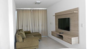 Un salon moderne avec un téléviseur à écran plat fixé à un mur en bois, un canapé beige et une grande fenêtre avec des rideaux.